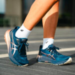 WhatsApp_Image_2025-05-15_at_12.33.07 | UAE SPORT STORE Close-up of blue ASICS running shoes on a person’s feet, wearing white socks, standing on a track surface.