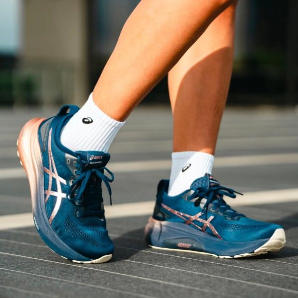 Close-up of blue ASICS running shoes on a person’s feet, wearing white socks, standing on a track surface.