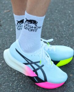WhatsApp_Image_2025-05-19_at_12.08.56 | UAE SPORT STORE Pair of white running shoes with neon pink outsoles on a dark asphalt surface, worn with white ribbed socks.