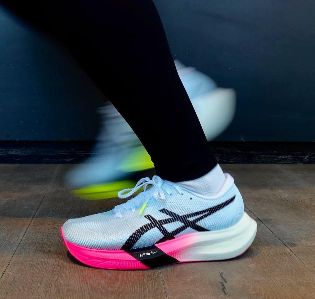 Close-up of a white running shoe with pink and neon accents in mid-step, motion blur showing forward movement.