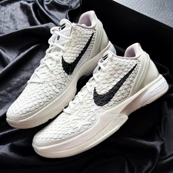 White Nike sneakers with a raised bubble texture and a black swoosh on a black fabric backdrop.