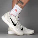 White Nike basketball sneakers with a star-patterned upper and black swoosh, worn on a model's foot with white crew socks.