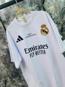 White Real Madrid soccer jersey on a hanger with Emirates Fly Better sponsor and club crest visible on the chest area, Adidas logo on the left.