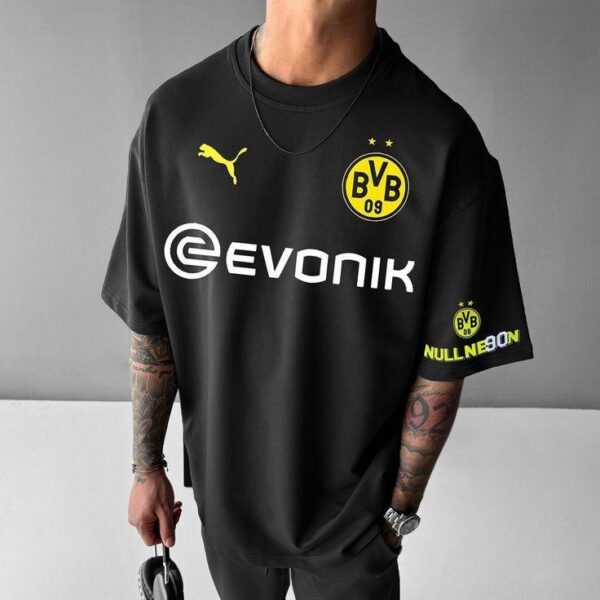 Person wearing a black Borussia Dortmund soccer jersey with Evonik sponsor and yellow club crest, standing against a gray wall.