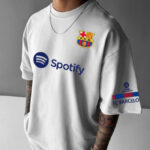 Man wearing a white FC Barcelona jersey with Spotify sponsor logo, featuring club crest on the chest and a La Liga patch on the sleeve.”] ,