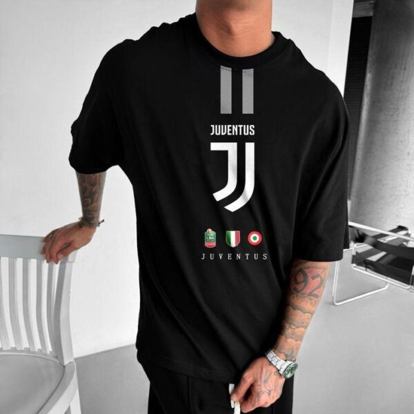 Man wearing a black Juventus t-shirt with the club logo, standing next to a white chair outdoors, tattoos visible on his arm and wristwatch on his wrist.