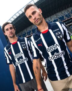 Two men in navy and white striped soccer jerseys posing side by side at a stadium.
