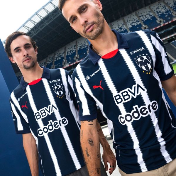 Two men in navy and white striped soccer jerseys posing side by side at a stadium.
