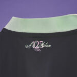 Close-up of the back of a dark polo shirt with a pastel collar and a decorative logo that reads 'A. Milan' and 'YEARS'.