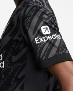 XIKUErJjHB2bUCW_c659effa-cd9a-438b-912f-dfb1fdbd003e | UAE SPORT STORE Close-up of a dark camouflage athletic shirt sleeve with a white Expedition logo.