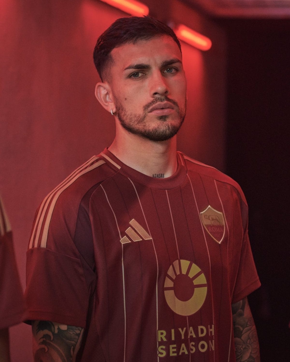 Portrait of a man with short dark hair and a beard wearing a maroon striped football jersey under red neon lighting