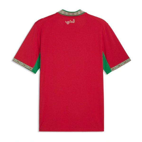 Back view of a red Moroccan-style tunic with green side panels and decorative patterned trim at cuffs and collar; Arabic script on upper back.