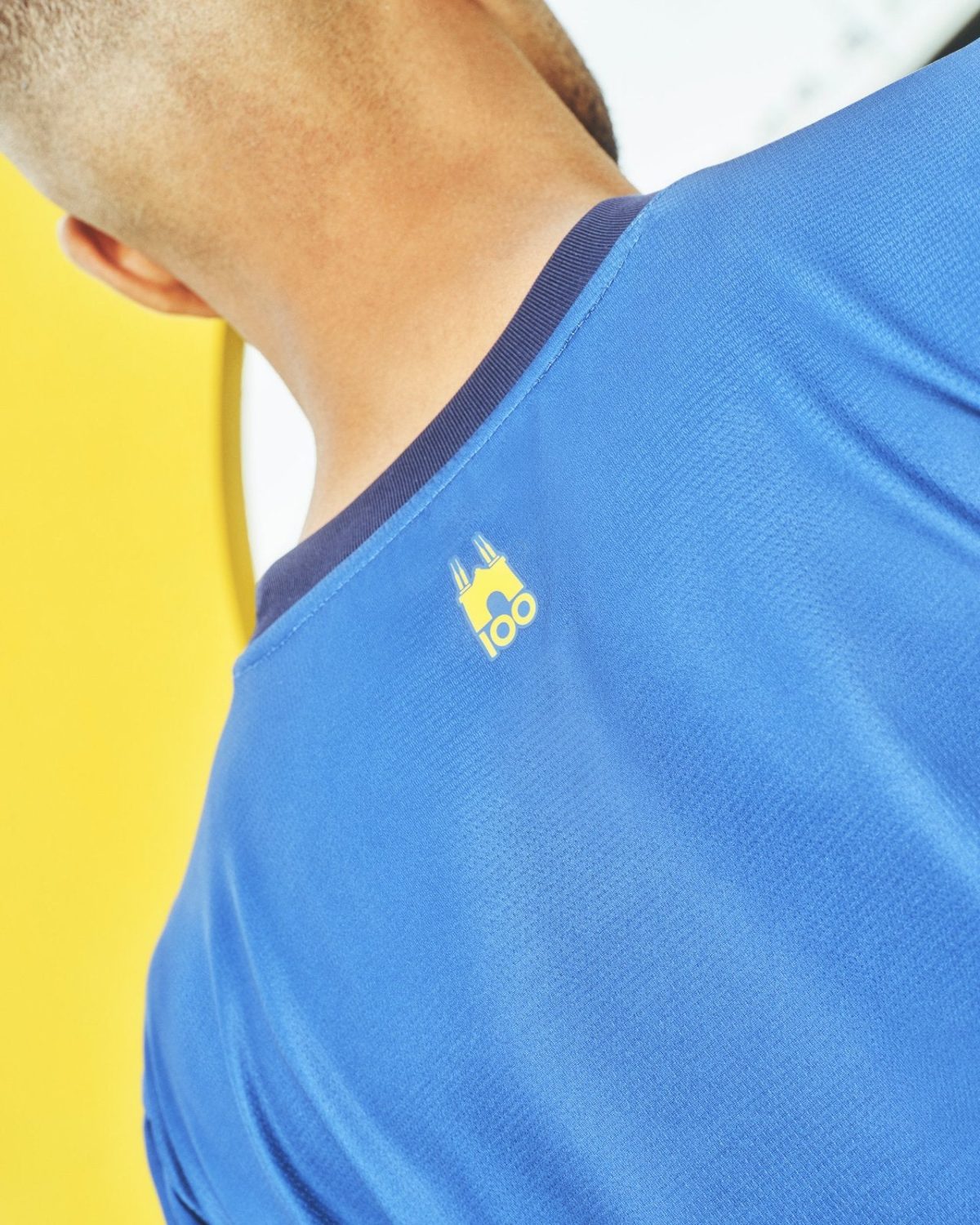 Close-up of a blue athletic shirt with a small yellow logo at the neckline.