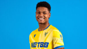 Smiling young man in a yellow sports jersey against a solid blue background.
