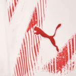 Close-up of a red Puma logo embroidered on white fabric with red graphic stripes in the background