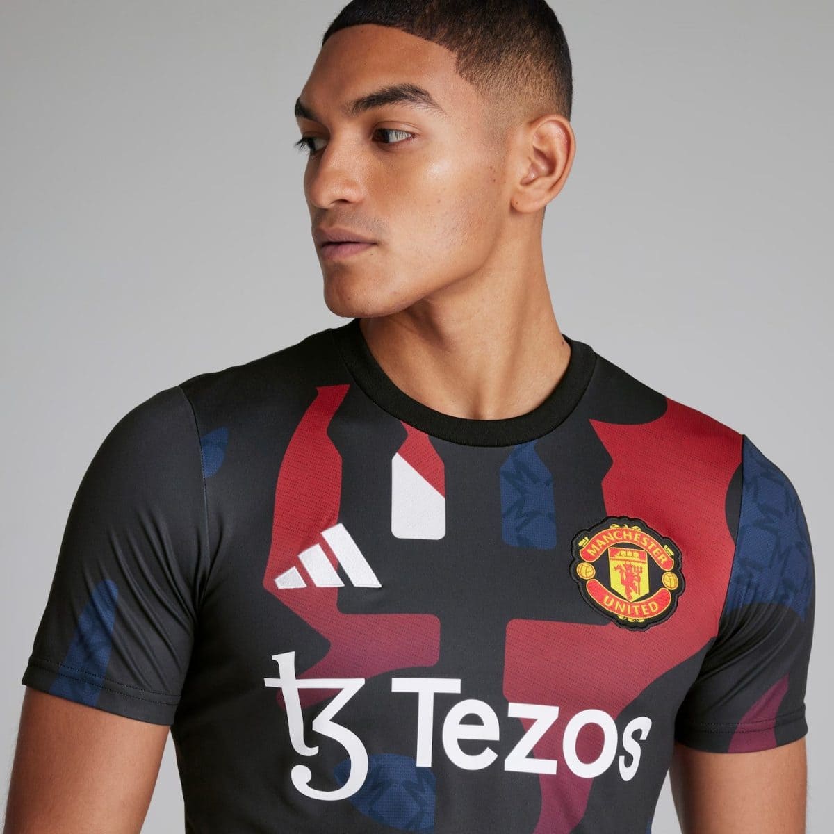 Side-profile of a man wearing a black Manchester United football jersey with red/blue graphic pattern and Tezos sponsor text, looking to the left