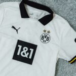 White Borussia Dortmund football jersey with black collar, crest, Puma logo, and race bib number 18 on it.