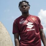Young man wearing a maroon Torino FC soccer jersey with Suzuki sponsor, standing against a clear blue sky.