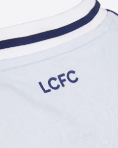 Close-up of a white jersey neckline with navy trim and the letters LCFC printed on the chest area