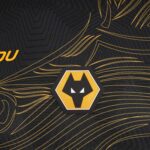 Close-up of a hexagonal yellow and black wolf head emblem on a black patterned fabric with gold lines, likely a team logo.