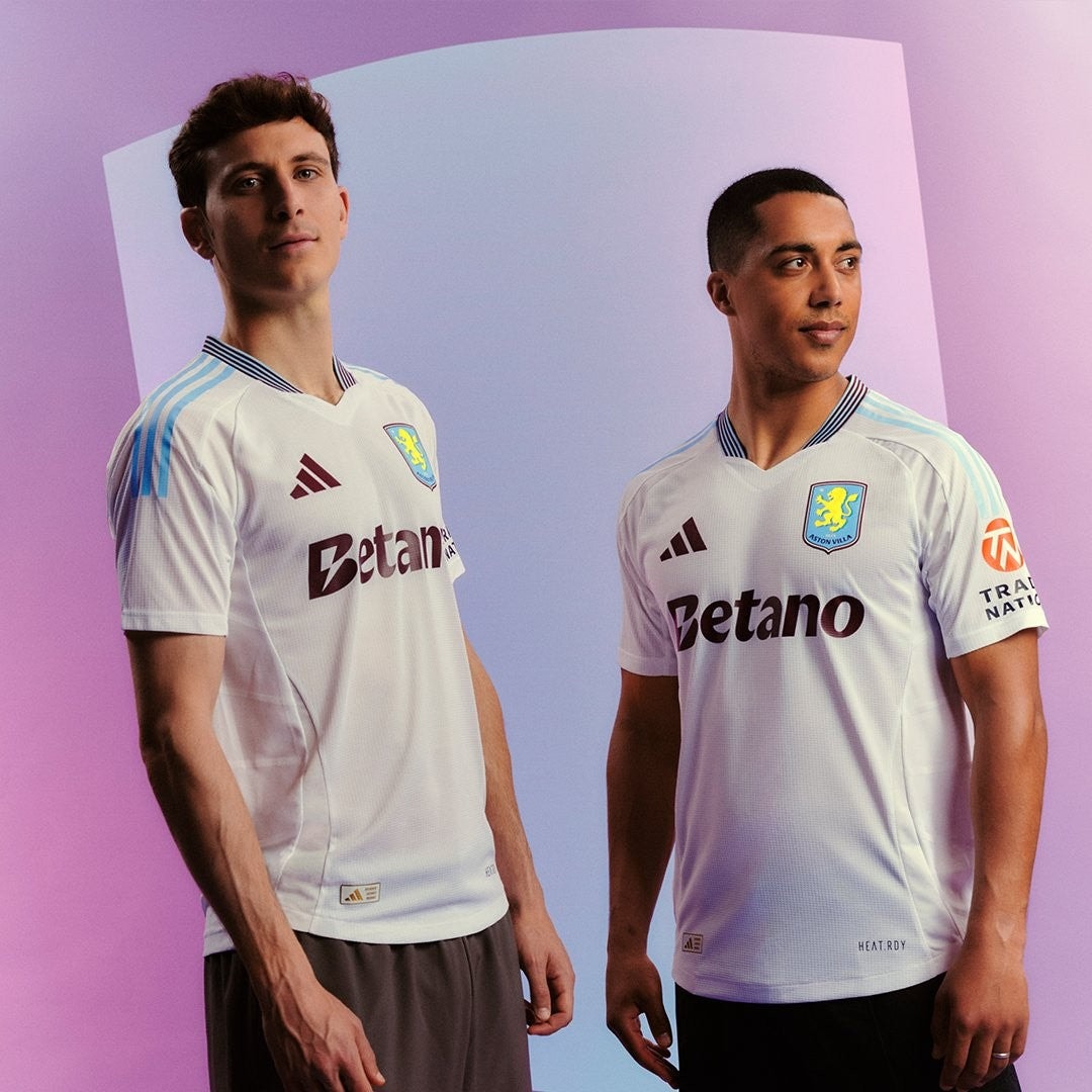 ZRCoX6pbEeblfO7 | UAE SPORT STORE Two men pose in white Aston Villa jerseys with Betano sponsor against a pink‑purple gradient backdrop.