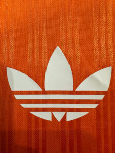 White Adidas trefoil logo on orange fabric background