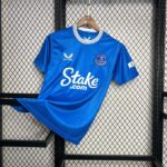 Blue Everton FC football jersey on a hanger against a wire-mesh backdrop, featuring Stoke.com sponsor text on the front.