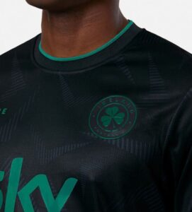 Close-up of a dark sports jersey with green trim and a circular crest featuring a shamrock on the chest area