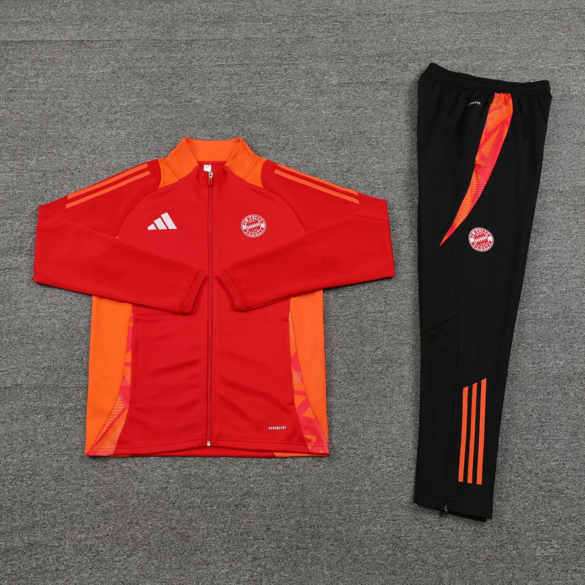 Red FC Bayern Munich jacket with zipper, paired with black track pants featuring orange side stripes on a gray carpet.