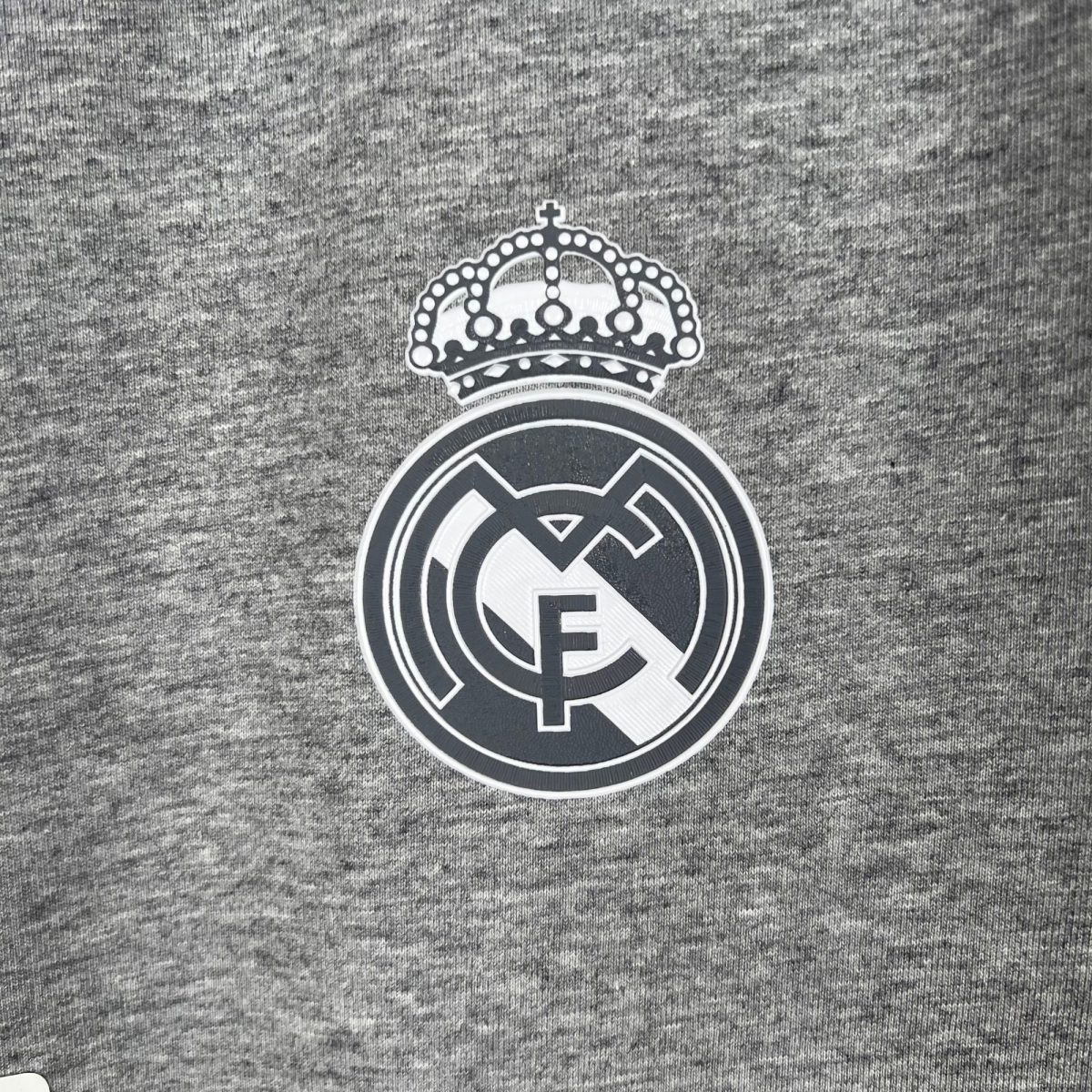 Partial Real Madrid crest visible on gray fabric background.