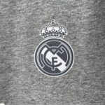 Partial Real Madrid crest visible on gray fabric background.