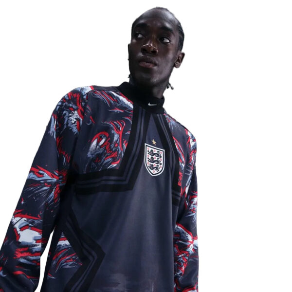 Young man wearing a dark England football jersey with a red-blue patterned outer layer, looking off to the side.