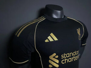 Black Liverpool FC soccer jersey on a mannequin with gold Adidas logo and 'Standard Chartered' sponsor on the front.