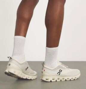 Light gray On running sneakers with a chunky white sole, worn with white crew socks; person standing sideways.