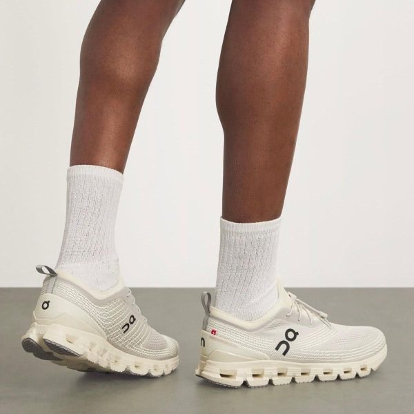 Light gray On running sneakers with a chunky white sole, worn with white crew socks; person standing sideways.