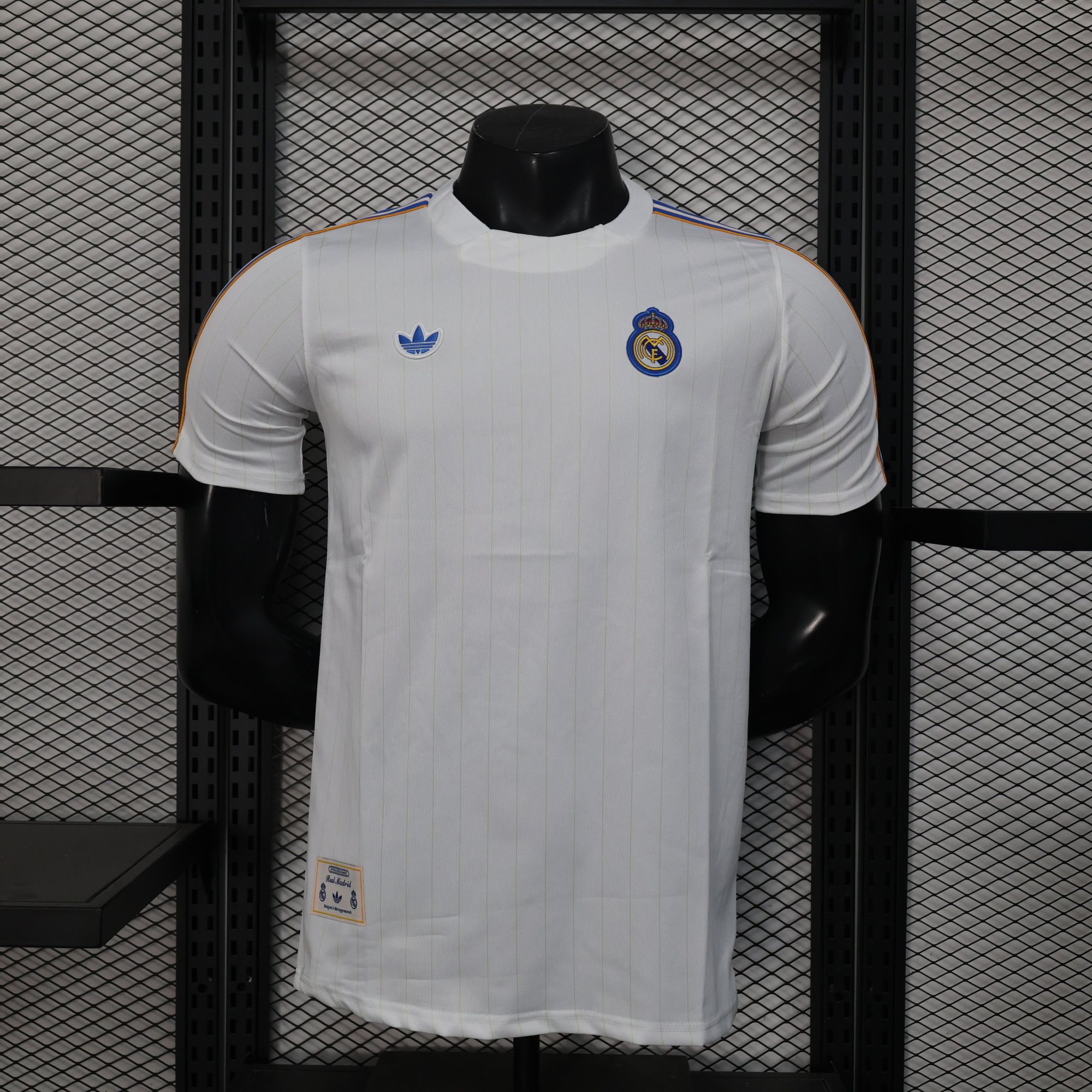 a1ca8dea | UAE SPORT STORE White Real Madrid soccer jersey on a black mannequin, crest visible on left chest and blue Adidas logo on the right, orange piping along shoulders, store display rack in background