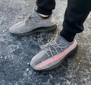 Person wearing gray knitted sneakers with a pink stripe, standing on frosted asphalt.