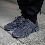 Close-up of dark gray running shoes on a concrete sidewalk, worn with black pants.