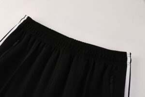 Close-up of black athletic track pants with an elastic waistband and white side stripes, showing zippered pockets on each side.
