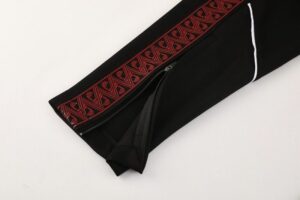 Black sleeve with a red embroidered stripe and zipper detail, likely part of a traditional or athletic garment surface.