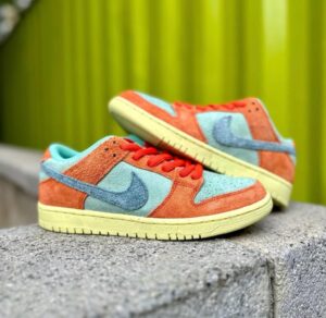 Pair of colorful suede sneakers in coral and blue resting on a concrete ledge with a bright green background.