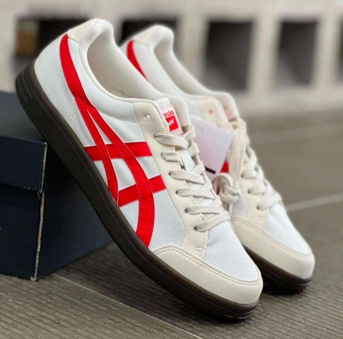 White sneakers with bold red side stripes and a black sole, angled on a dark box.