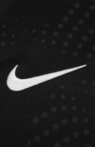 White Nike swoosh embroidered on black dotted athletic fabric.