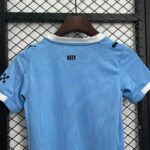 Light blue athletic jersey on a wooden hanger, displaying a 'CITY' label, with dark brand marks on the shoulders, hanging in front of a metal chain-link fence.