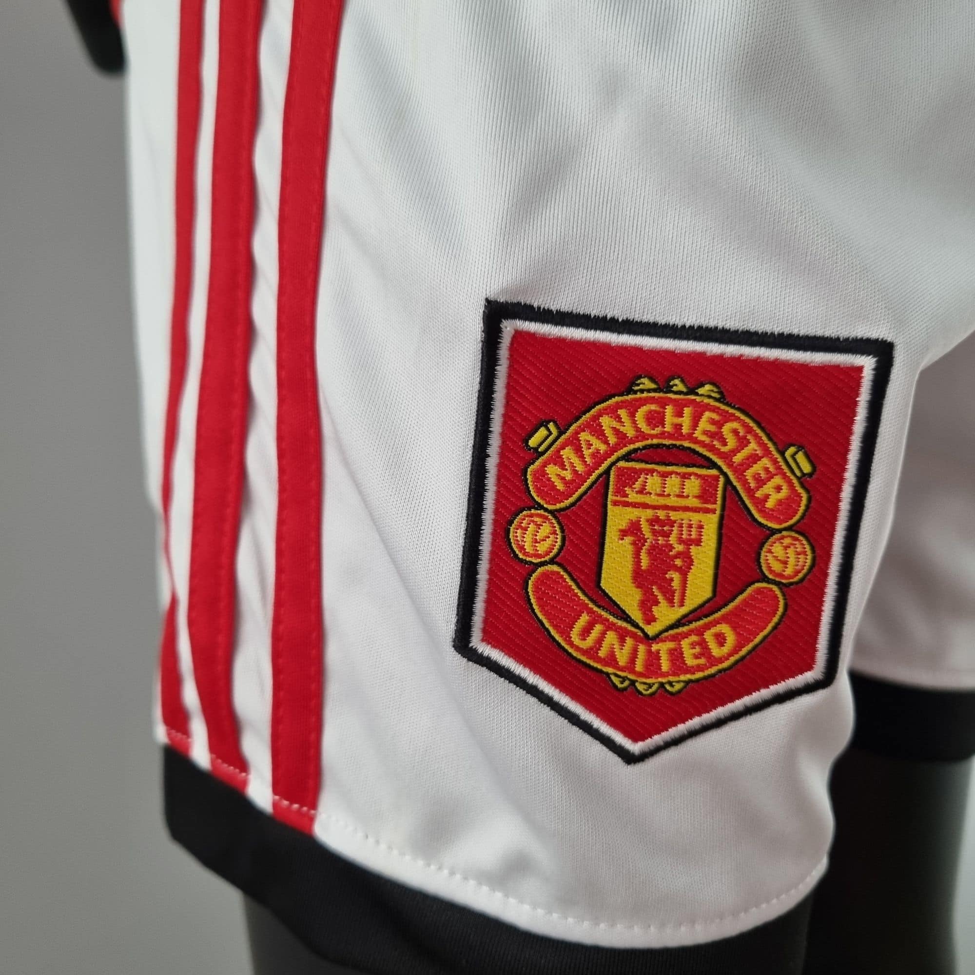 a5f2b827_595b632e-7966-4d55-9bbf-a7eceeb95cf7 | UAE SPORT STORE Close-up of a white football jersey with red stripes and the Manchester United crest sewn on it.
