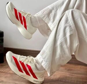 White sneakers with red stripes on both feet, propped up on a white sheet-covered surface.