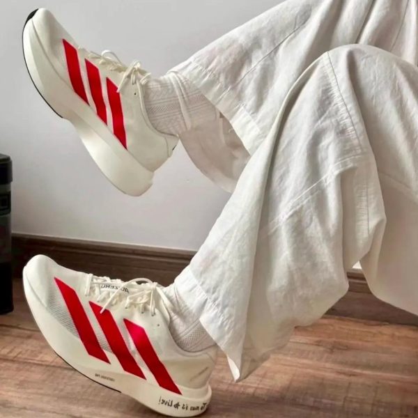 White sneakers with red stripes on both feet, propped up on a white sheet-covered surface.