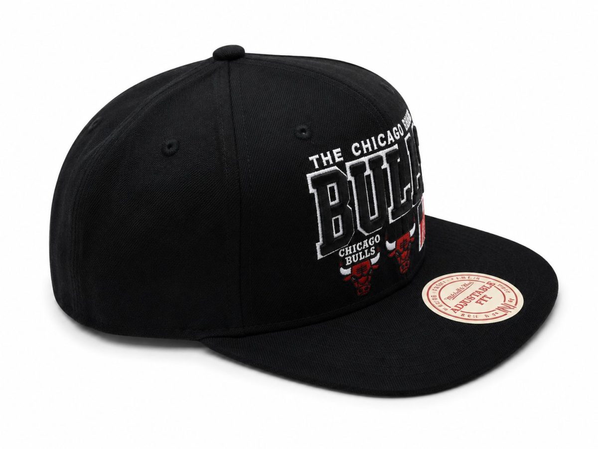 Black snapback hat with Chicago Bulls embroidery and red bull logos on the front panel, curved brim visible, sticker on brim says Adjustable Fit.