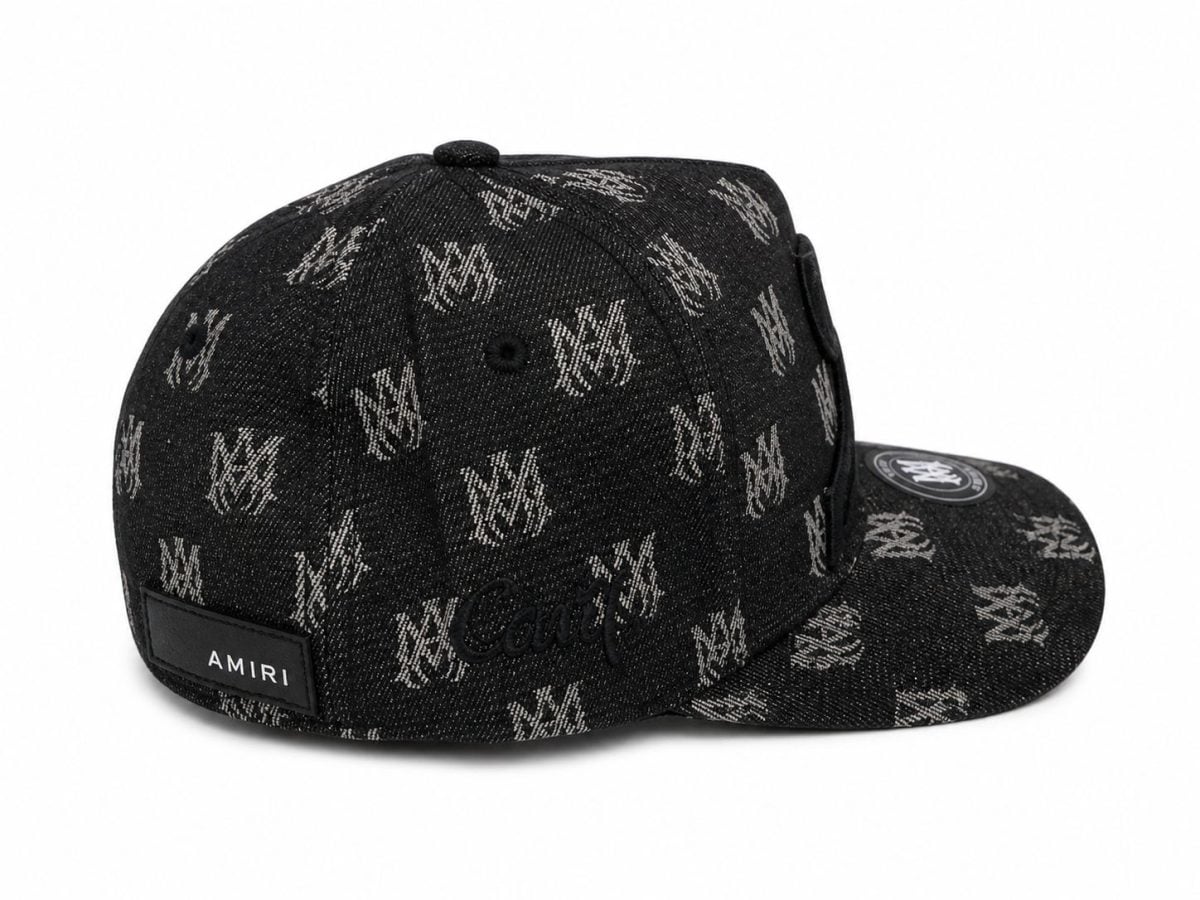 Black denim cap with a repeating white logo pattern and an Amiri label on the back, curved brim with a circular patch on the top.
