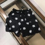 Black swim shorts with an all-over white interlocking logo pattern and an elastic waistband with a back pocket visible.